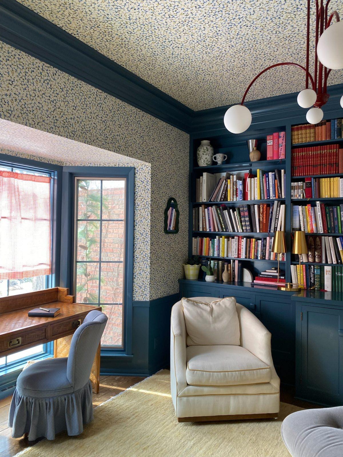 Home office with blue trim and bookshelf cabinetry, floral wallpaper, a cream rug, swivel chair, desk, and blue ruffled desk chair.