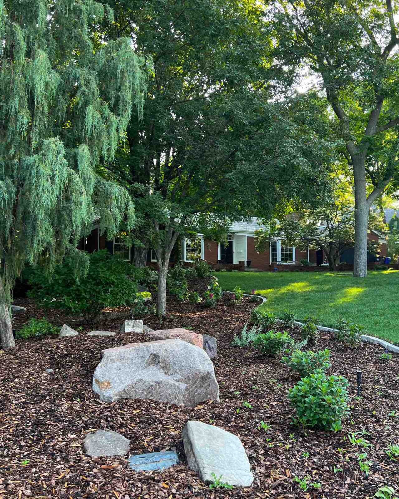 A gravel and rock garden surrounded by lush willow trees and grass