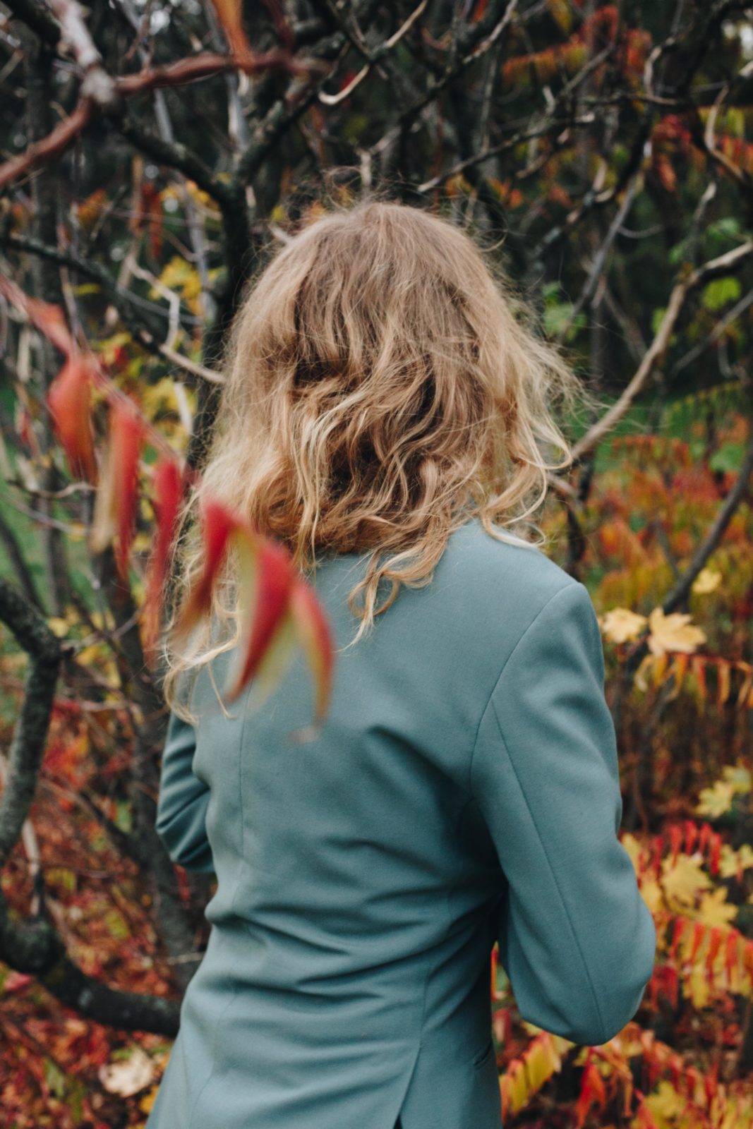 Woman standing in fall foliage, wearing a light blue blazer.