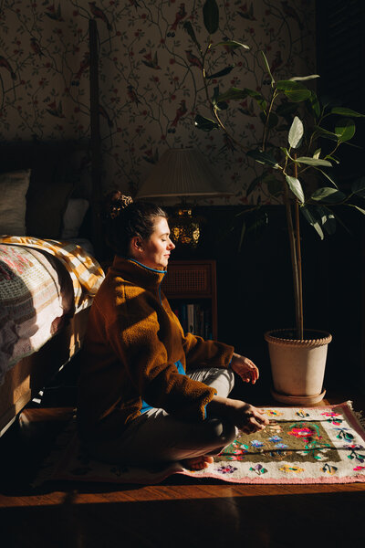 Woman sitting on the floor in the bedroom, with eyes closed meditating