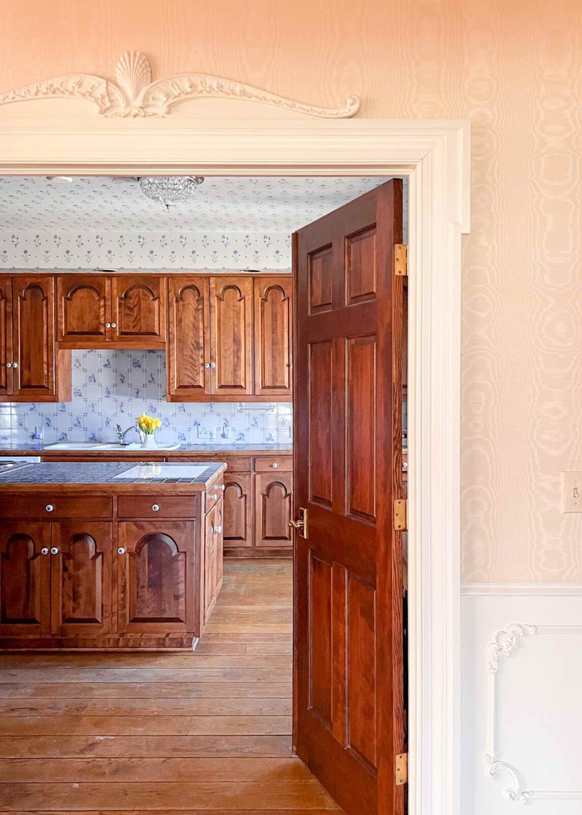 Kitchen with dark wood cabinets, wood flooring, Delft tile backsplash, blue tile countertops, and blue floral wallpaper on the ceiling