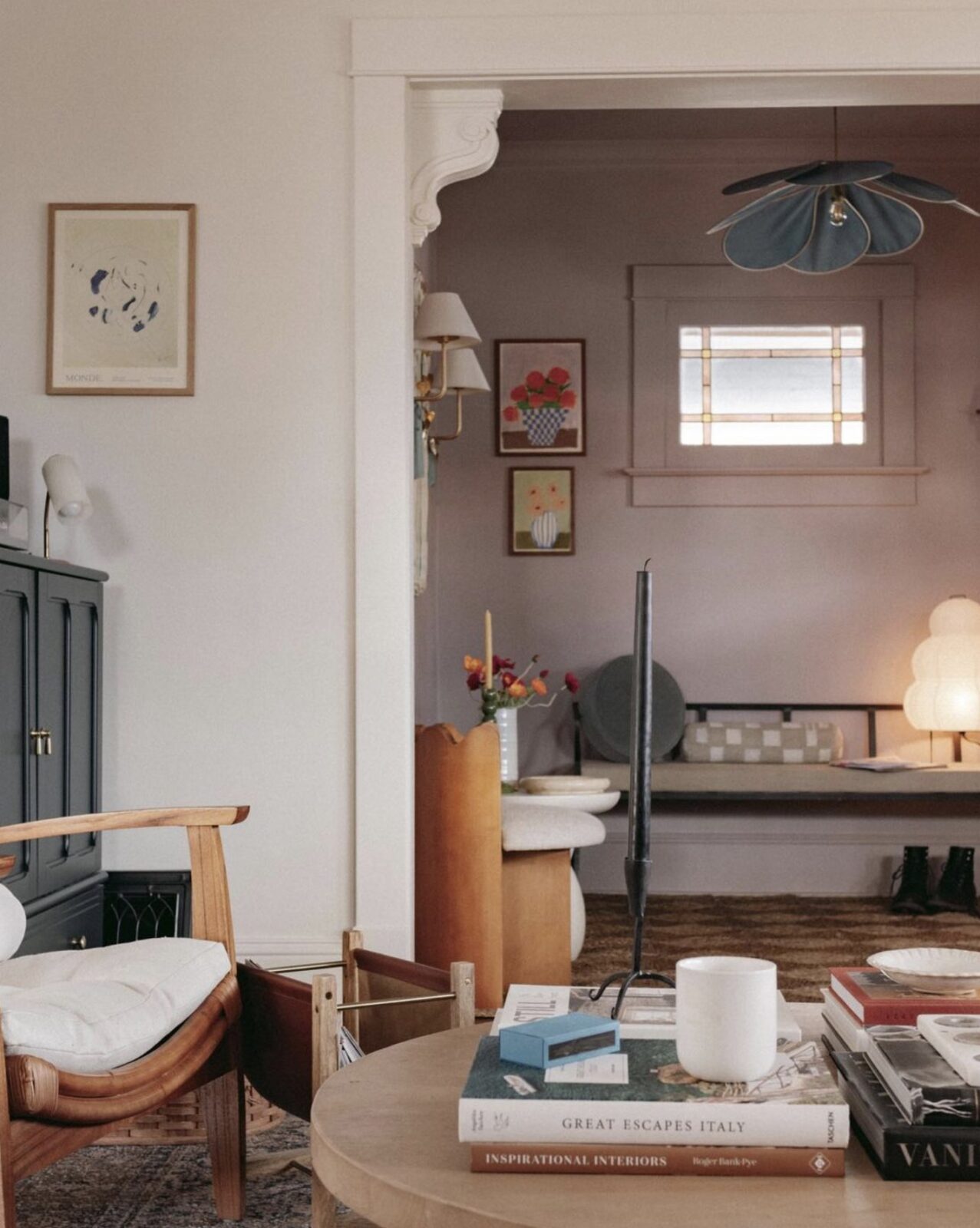 Living room with a round wood coffee table topped with design books, looking into an entryway with dusty pink walls