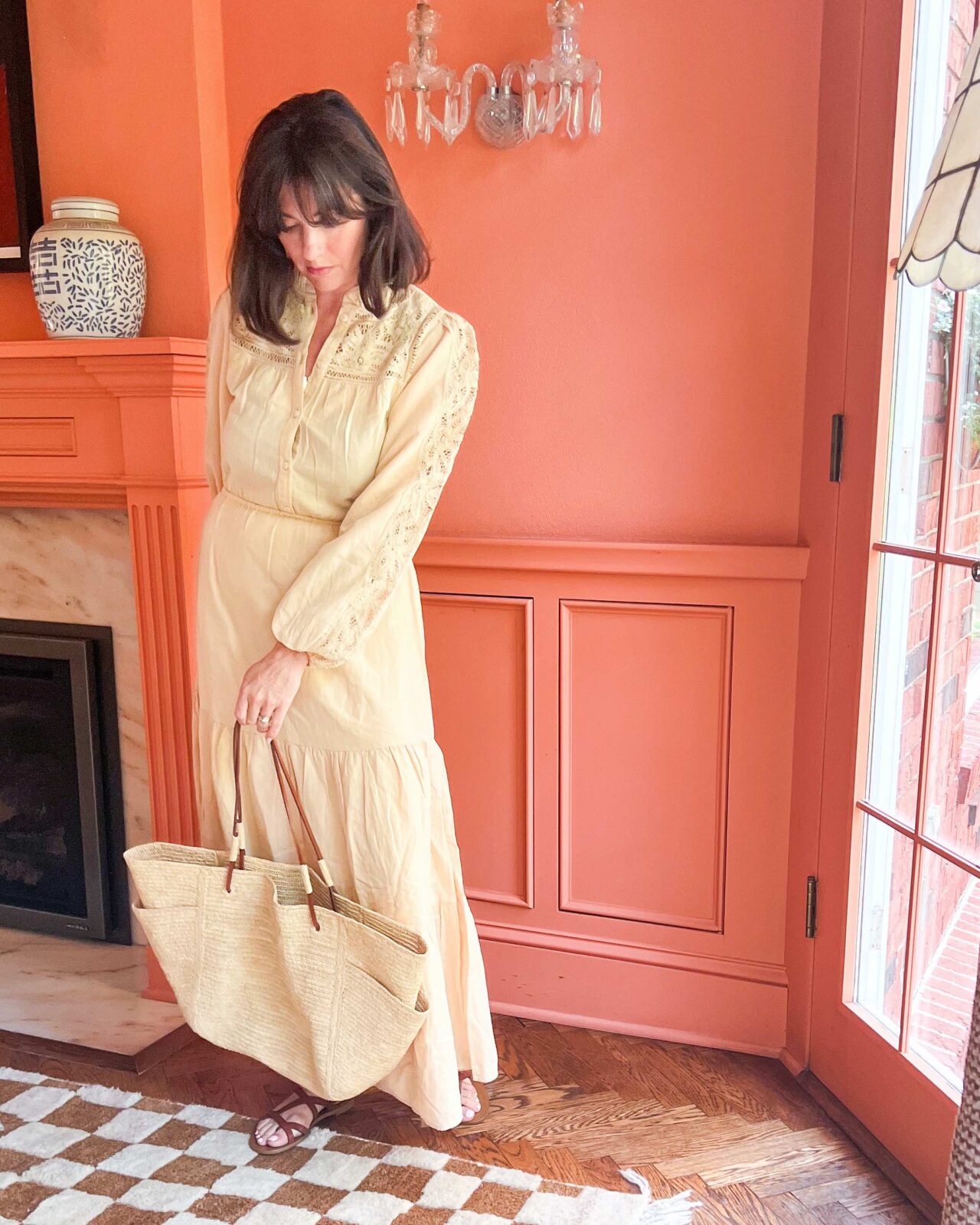 Woman wearing a long cream-colored dress and leather sandals, while carrying a large tote bag.