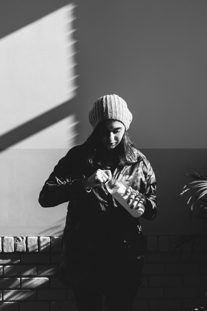 Woman getting ready to go for a run, wearing a hat and jacket, holding a water bottle.