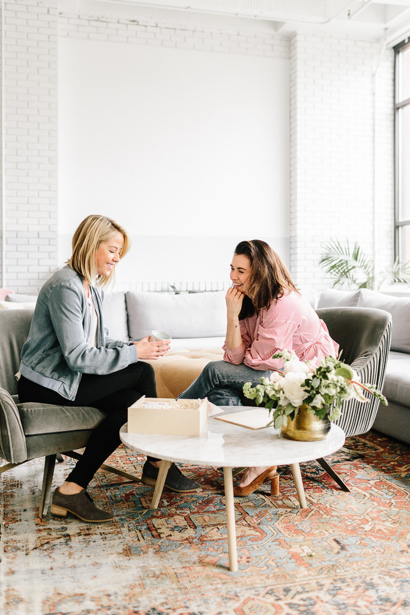 Two women sitting next to a coffee table and laughting